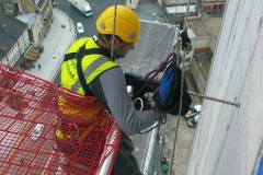 Rope access technician drilling side of building.